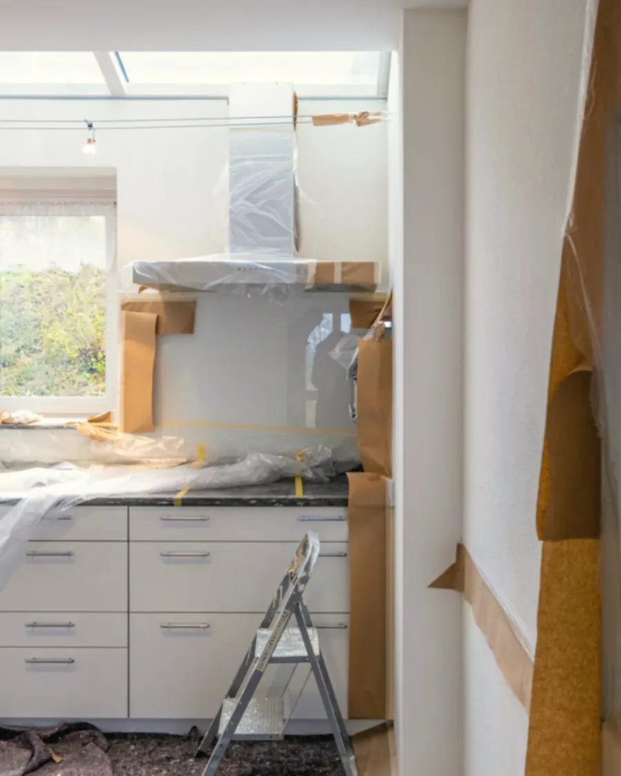 A kitchen in the middle of a renovation, counters under plastic sheeting, lit by a window and a skylight.