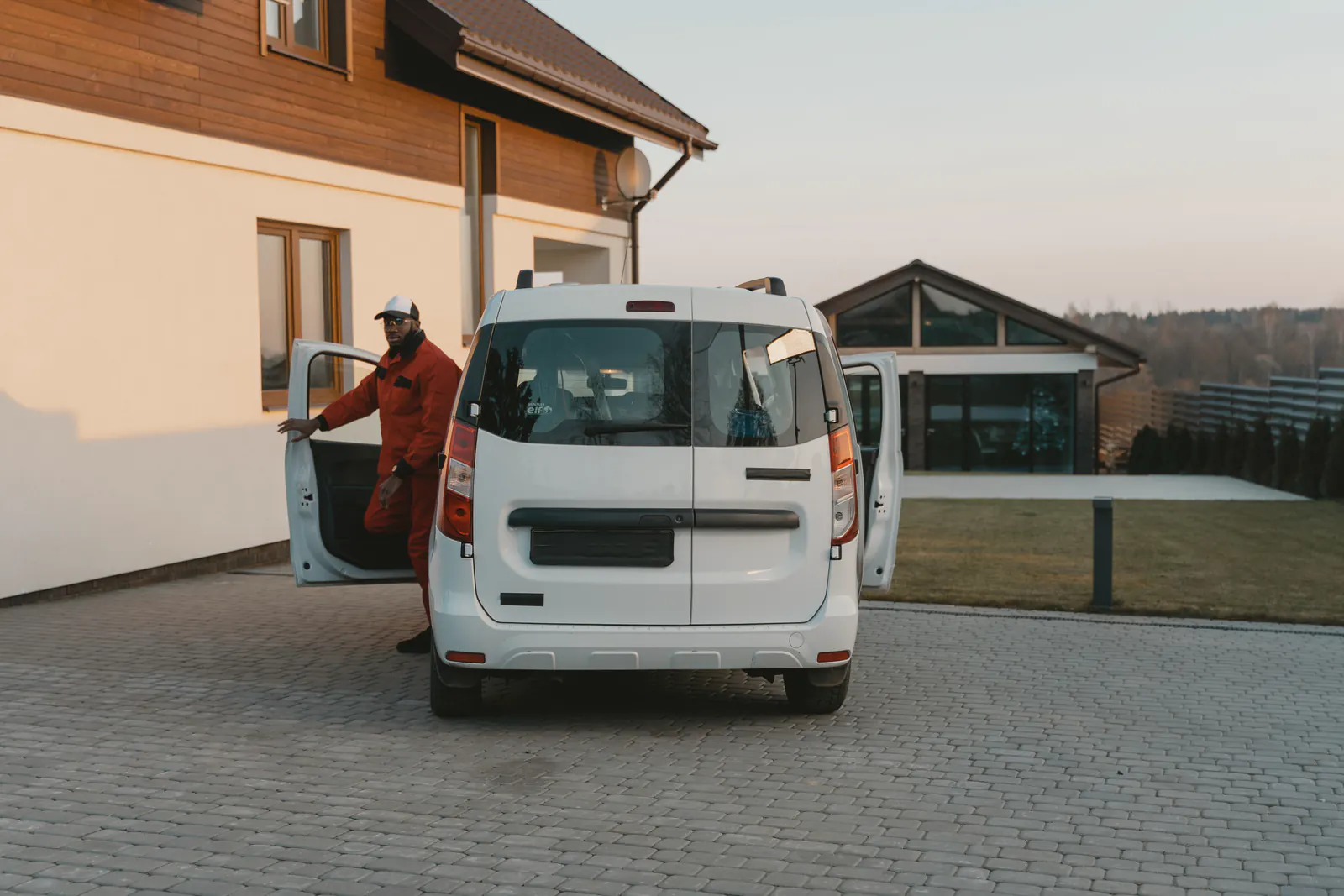 Worker in uniform stepping out of a white van parked in front of a modern house.