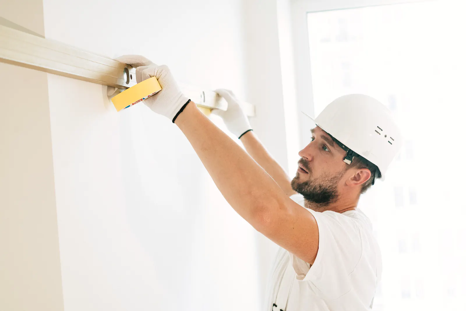 Builder in a hard hat checking a wall with a spirit level indoors.